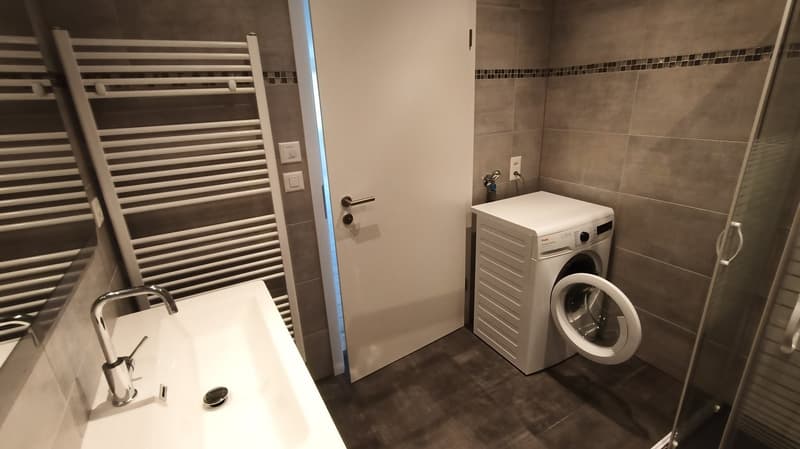 modern white tiled bathroom with washing machine, faucet, mirror, radiator