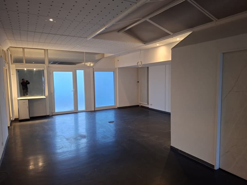 Empty room with glass doors and large windows, black flooring, a radiator, a small cabinet, a crack on the wall