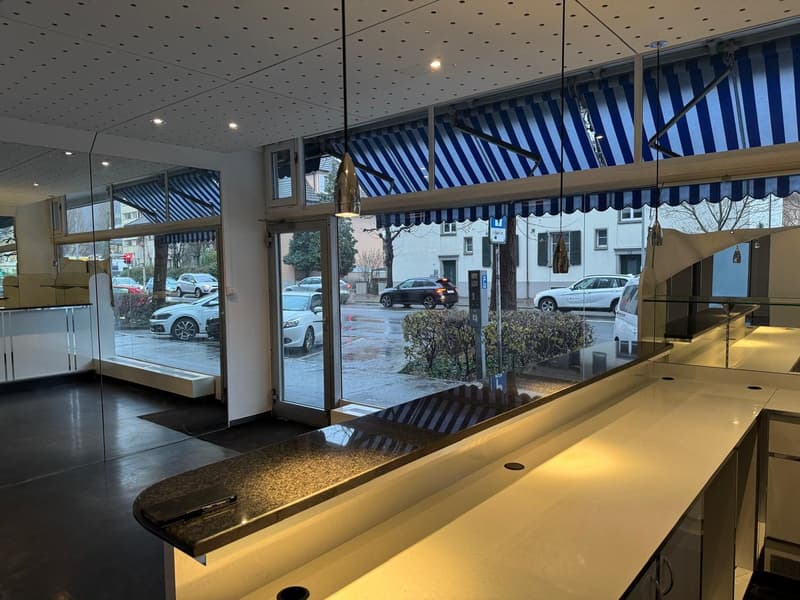 Glass storefront, black floor, shiny white countertops, modern lamps, cars parked outside