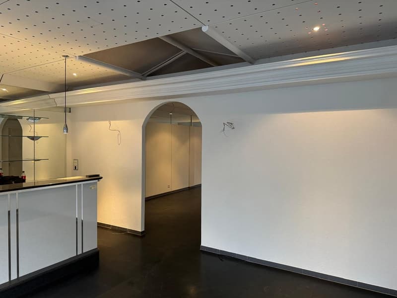 empty room, white walls, arched entry, black floor, counter, suspended lights
