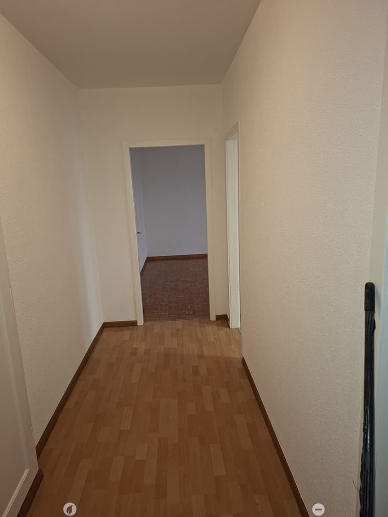 Empty hallway with wooden floor and two doors, one of which leads to a room with wooden parquet floor