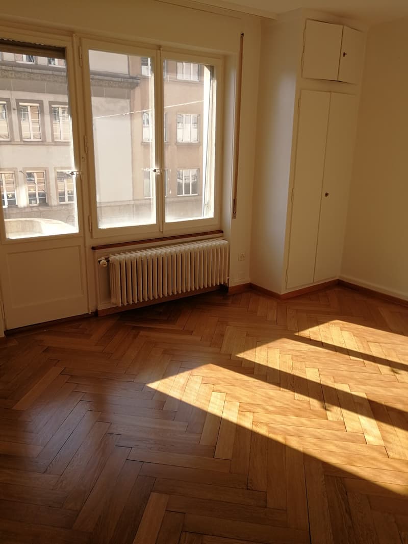 empty room, wooden parquet flooring, large windows, wooden door, white radiator, wooden built-in closets, power outlet