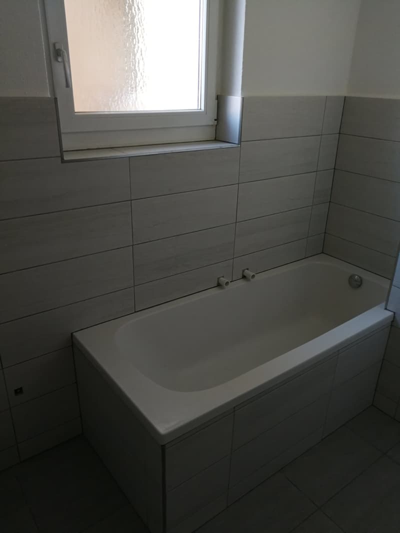 Bathroom with a bathtub, tiled walls, and a window above the tub