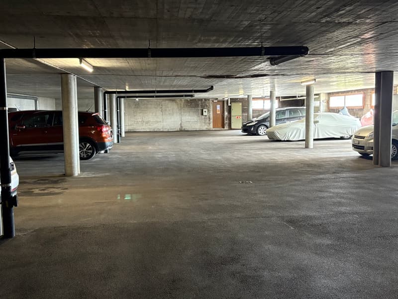 Indoor parking garage with concrete floor, concrete ceiling, and several parked cars