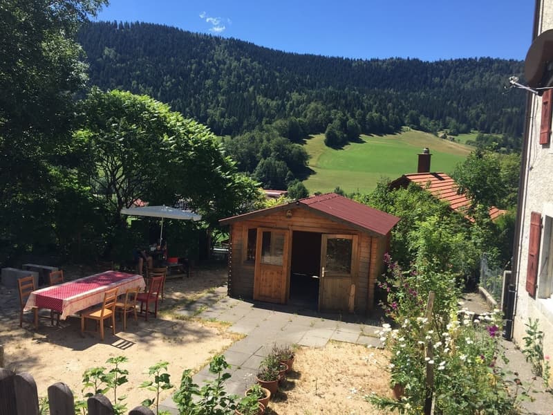 small garden with table and chairs, small wooden cabin with door, greenery and plants, beautiful mountain view