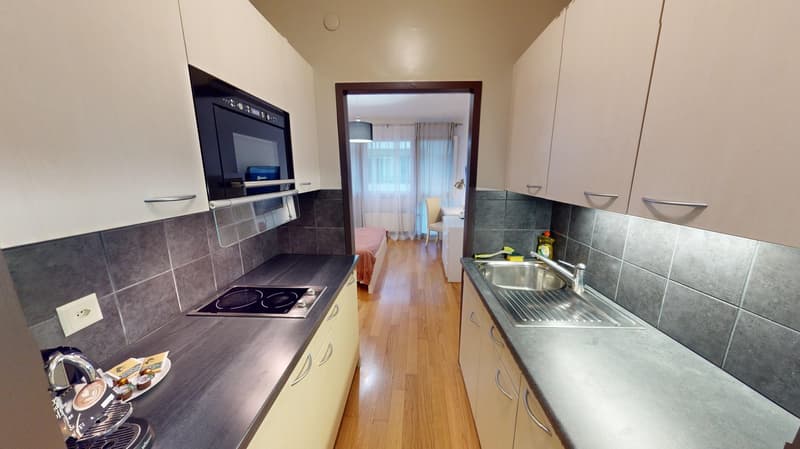 Modern kitchen with a dishwasher, induction stove, oven, kitchen cabinets, gray countertop, a sink, and an electrical outlet.