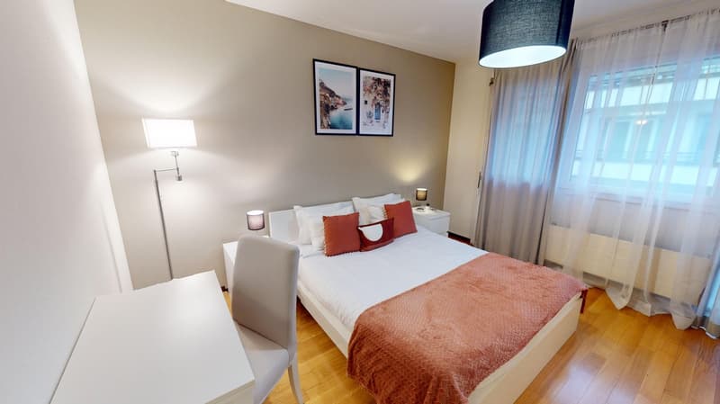white double bed with pillows, gray desk and chair, white nightstands, white wall, wooden floor, lamps, picture frames, curtains, window