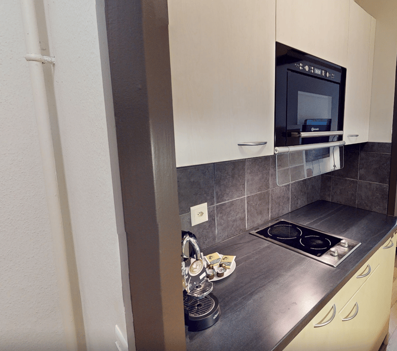 Kitchen with electric stove, built-in microwave, tiled backsplash, built-in cabinets, countertop with plate and kettle