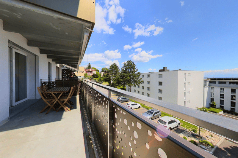 Modern balcony with table and chairs, metal railing, view of greenery