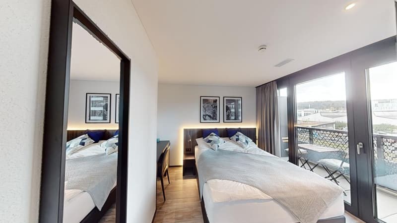 Two twin beds, headboards with storage boxes, large windows, balcony with outdoor seating, mirror, desk