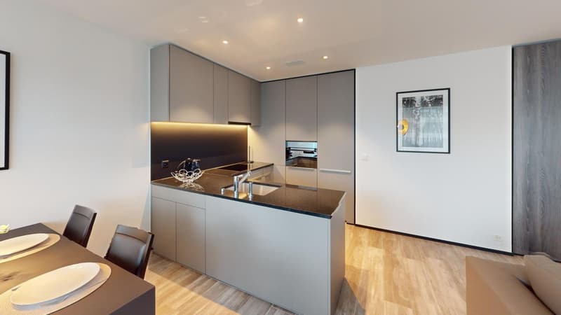 Modern kitchen with gray cabinets, black countertop, stainless steel appliances including a dishwasher, and hardwood flooring. The kitchen is open to a dining area with a table and chairs.