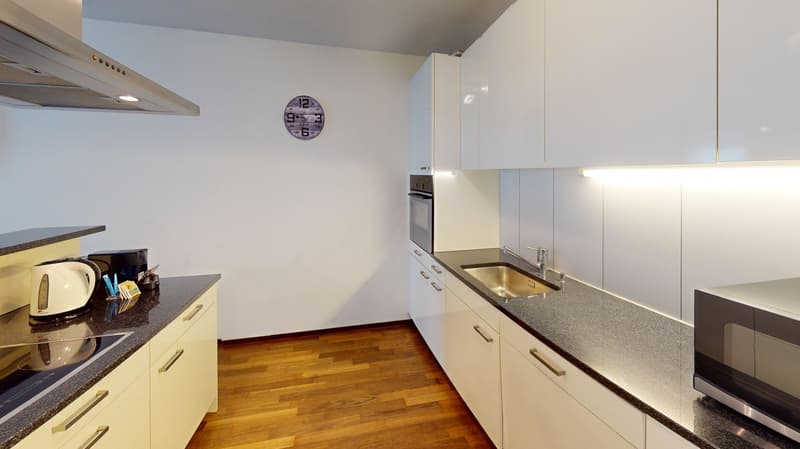 Modern kitchen with white cabinets, wooden floor, granite countertop, microwave, sink, faucet, kettle, clock, wall mounted oven