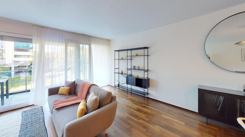 A gray couch with pillows, white curtains, and a balcony