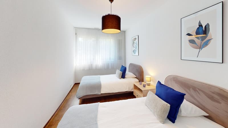 Two beds, white sheets, pillows, nightstands, lamps, artwork on wall, wooden floor, curtains on window