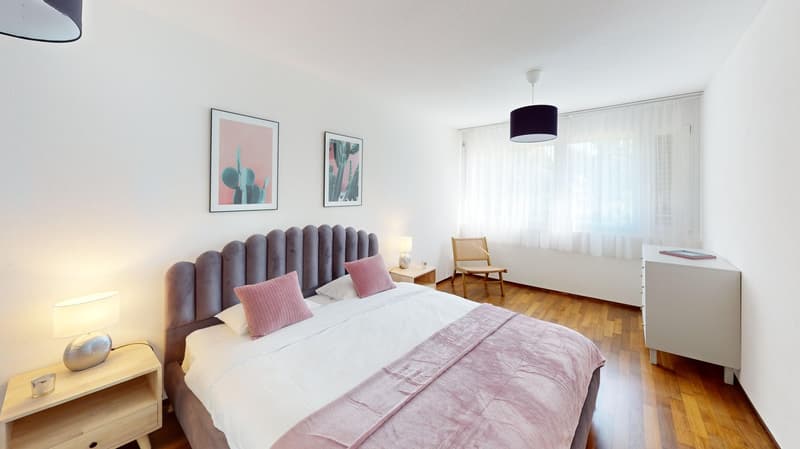 A bed with pink blankets, a wooden cabinet, and a chair near the window