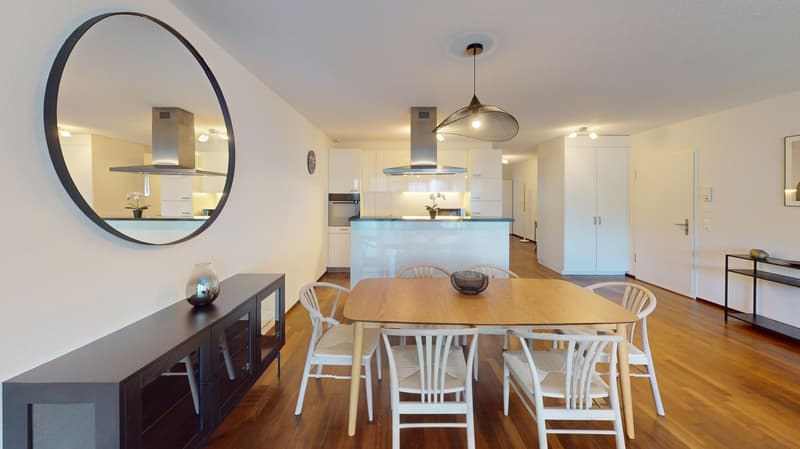 modern dining room with large circular mirror, wooden table, and white chairs
