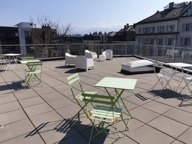 Modern outdoor terrace with white lounge chairs, green folding tables, railings, clear sky view.