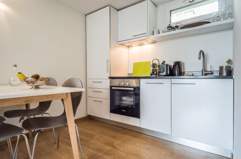 kitchen with wooden floor, dining table, modern cabinets, oven, faucet, toaster, coffee maker, and sink with dishwasher