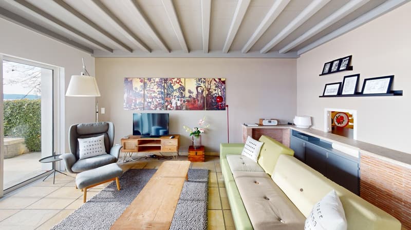 open living room, wooden floor, gray and yellow sofa, flat screen TV, entertainment center, dining table, coffee table, armchairs, decorative pillows, carpet, fireplace, windows with sliding doors