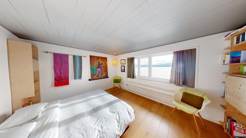 bed, white linens, chairs, radiator, window, curtains, art on wall, wooden shelves, books, decorative pillows