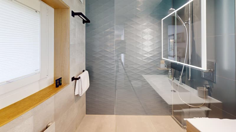 Geometric wall tiles, white bathtub, shower, mirror, wooden shelf