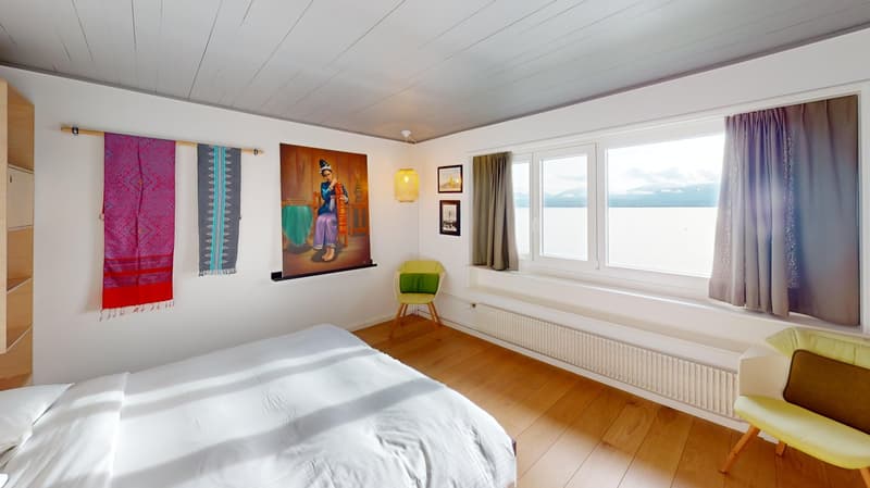 single bed, two decorative pieces on wall, yellow chair, wooden floor, large window with sea view, radiator