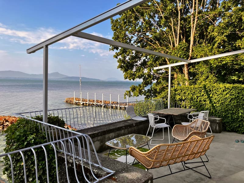 Outdoor area with chairs, table, plants, metal railing, shade structure, view of the sea