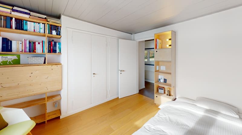 modern bedroom with a double bed, wooden floor, two white doors, bookshelf, radiator, power outlet