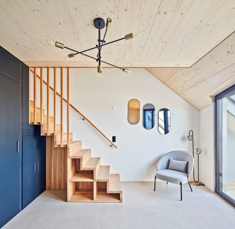 Open floor plan with white walls, hardwood floors, wooden stairs, open shelving, modern fixtures, round mirrors on wall, black round chairs, black floor lamp, wooden ceiling, glass door
