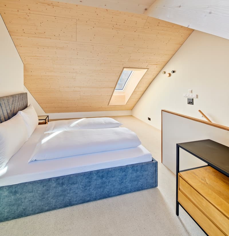 bedroom with a bed, white linens, blue headboard, white walls, wooden ceiling, nightstand, wall switches, and a skylight