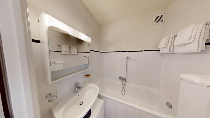 Bathroom with white tiles, bathtub, sink, mirror, and towels