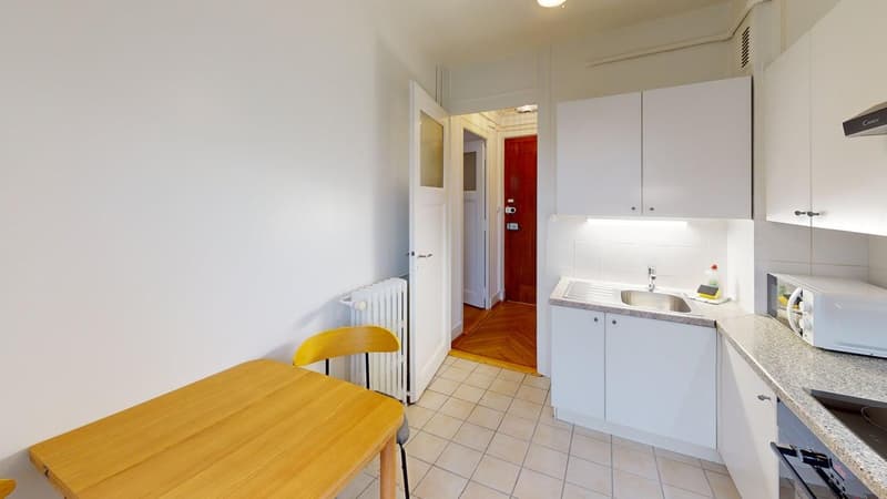 small kitchen with wooden table and chair, white cabinets, radiator, countertop with microwave and sink