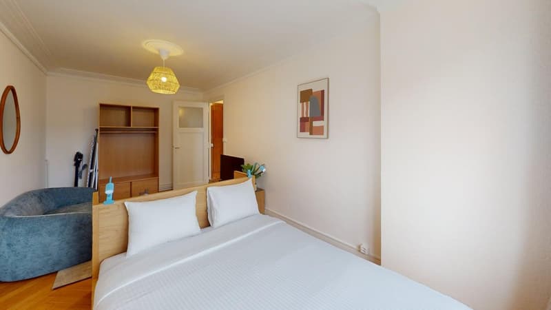 Double bed, white linens, wooden nightstands, round mirror, open closet, abstract painting, decorative plant, white radiator