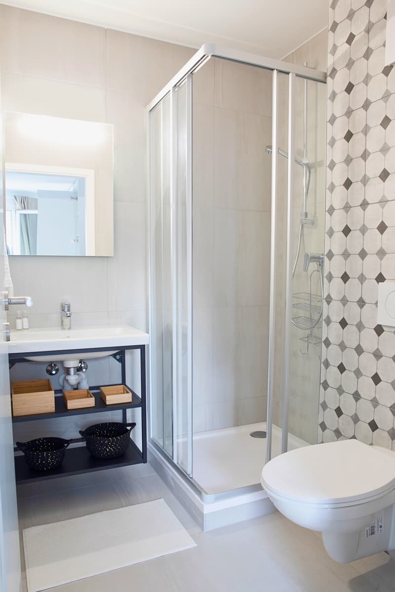 Modern bathroom with white tiles, shower, sink, and toilet