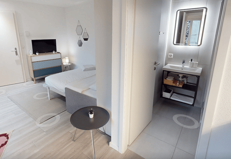 room with double bed, dresser, nightstand, lamp, carpet, TV, table, armchair, white sink with mirror, wall mounted outlet, round wall stickers