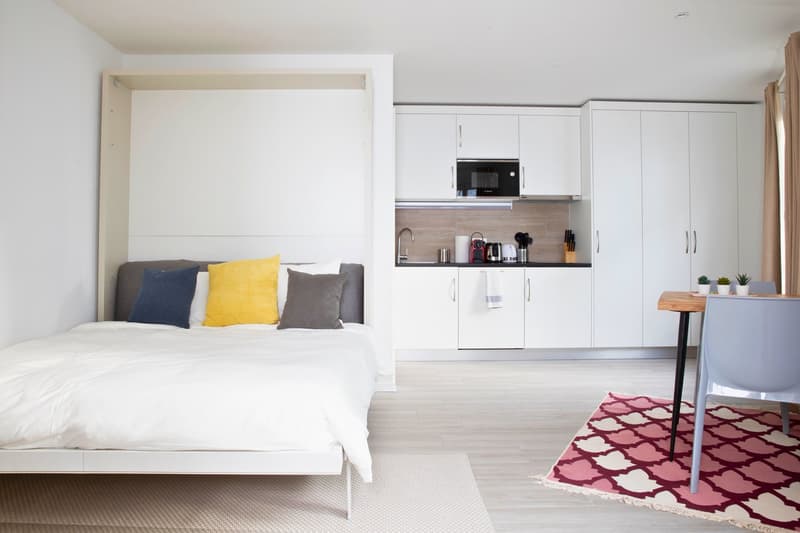 A small apartment, featuring a bed, a modern kitchen, and a dining area.