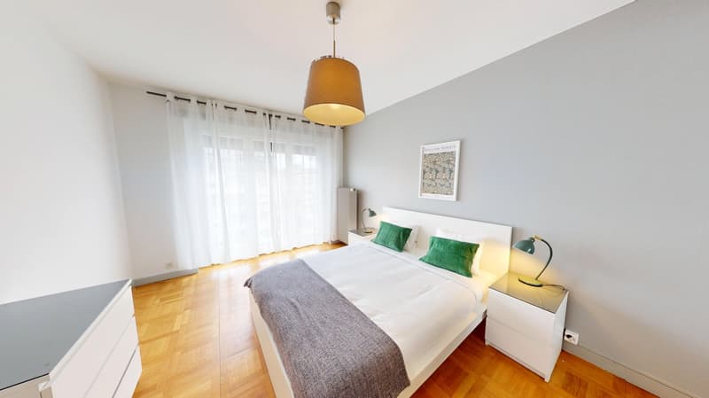 Bedroom with wooden floor, white walls, large bed, white nightstands, lamps, picture frame, white curtains