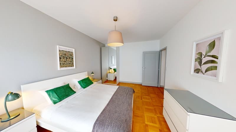 Bedroom with a bed, nightstands, lamps, a mirror, a wardrobe, and a wooden floor.