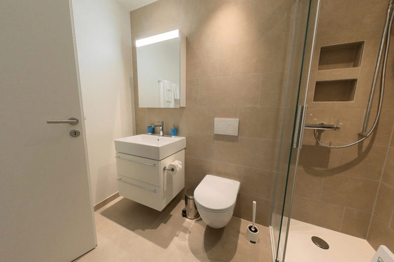 Modern bathroom with white vanity, toilet, glass shower enclosure, and beige tile walls.