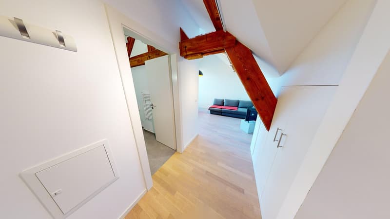 Wooden flooring, white walls, wooden beams, open doorway to living room with couch and TV