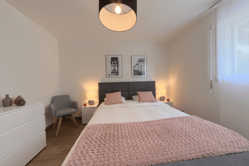 Bedroom with a double bed, nightstands, lamps, a chair, a dresser, and a window with curtains.