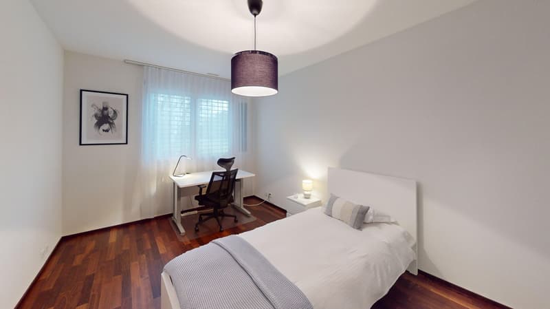 Spacious bedroom with hardwood flooring, white walls, large windows, a desk with a chair, and a pendant light fixture above the bed.
