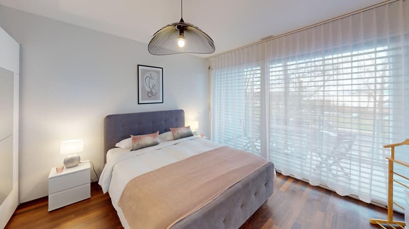 Spacious bedroom with large windows, hardwood floors, gray upholstered bed, bedside tables, and a pendant light fixture