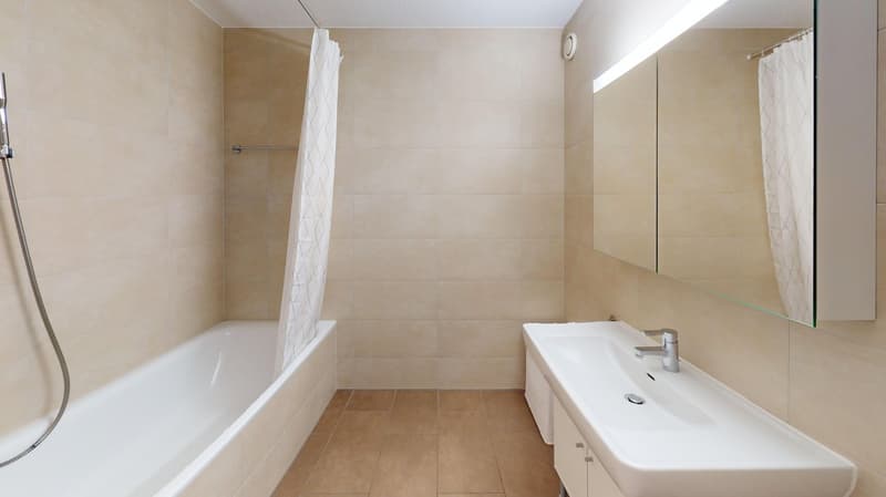 Spacious bathroom with beige tile walls and floors, a bathtub, a vanity sink, and a mirror cabinet.