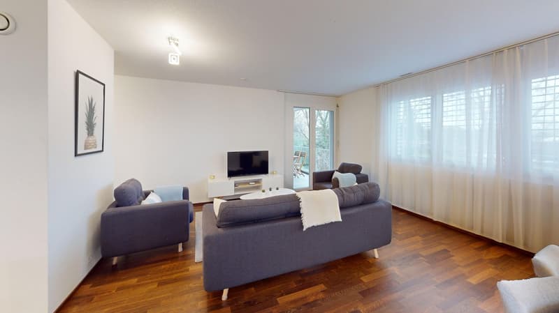 Spacious living room with hardwood floors, white walls, large windows, gray sofa set, TV stand, and a framed artwork on the wall
