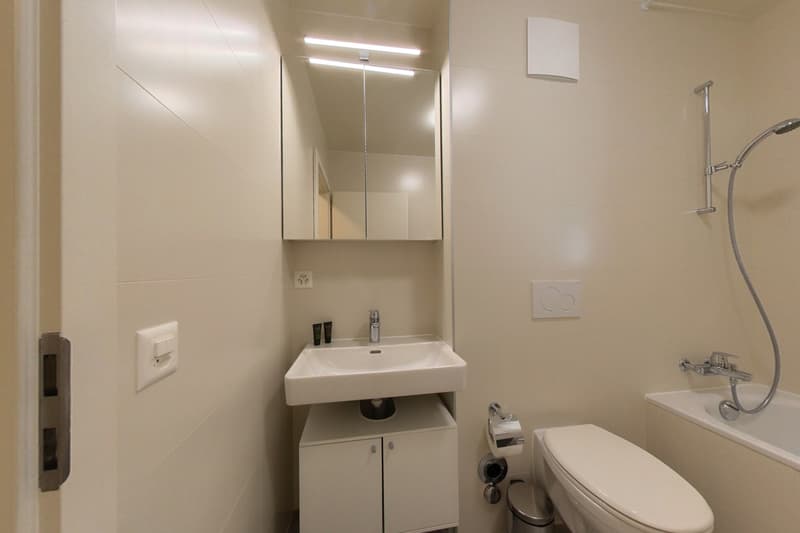 modern bathroom with white tiles, white sink, mirror, bathtub, toilet, and shower