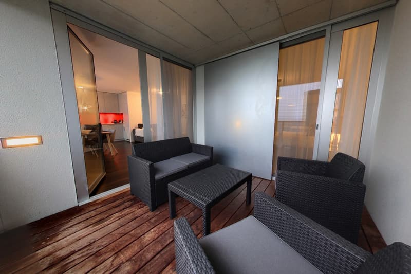 balcony with wooden floor, black wicker furniture, glass doors, sliding glass doors, kitchen visible through the glass
