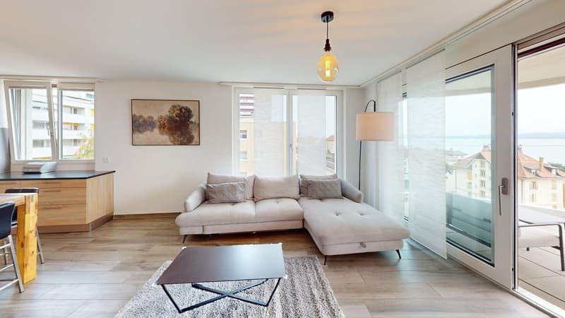 large L-shaped sofa, coffee table, rug, wooden floor, double doors to balcony, windows, painting, kitchen counter