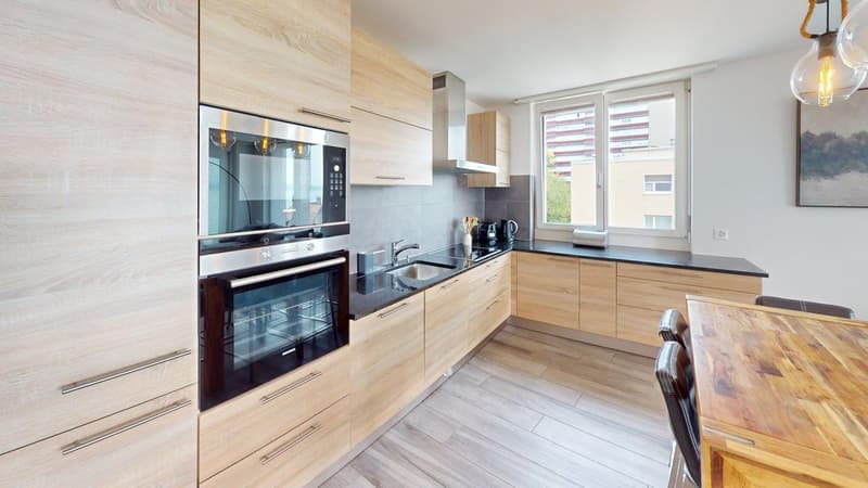 modern kitchen with wooden cabinets, black countertops, stainless steel appliances, and a wooden dining table