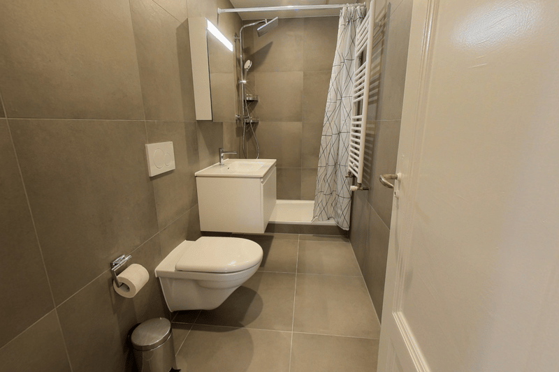A small bathroom featuring a toilet, shower, sink, and tiled flooring.